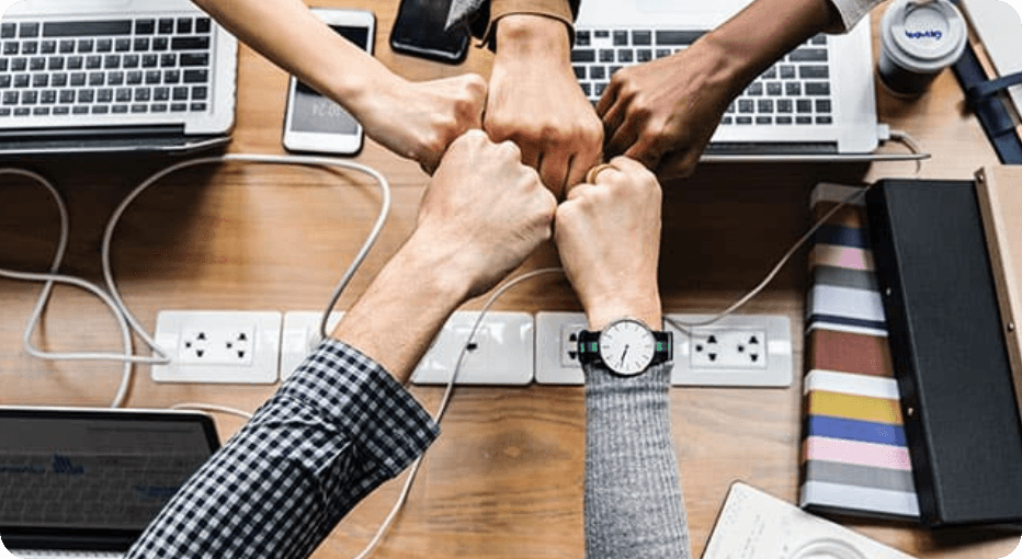 Team members bumping fists over a desk of laptops and phones